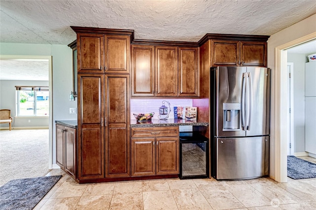 kitchen with a textured ceiling, tasteful backsplash, stainless steel fridge with ice dispenser, beverage cooler, and dark stone counters