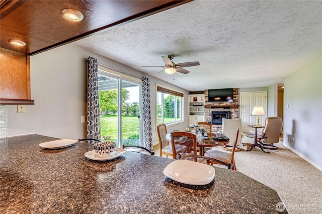 dining room featuring a large fireplace, ceiling fan, and a textured ceiling