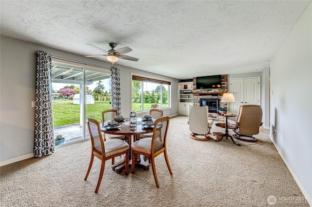 dining room with ceiling fan, light carpet, a fireplace, a textured ceiling, and baseboards