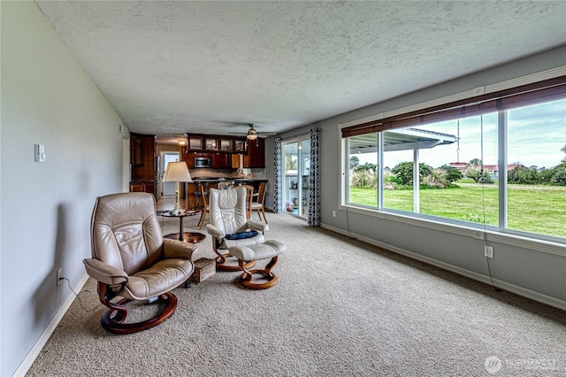 living area featuring baseboards, ceiling fan, light carpet, and a textured ceiling