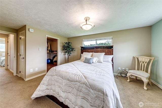 carpeted bedroom with a textured ceiling, baseboards, a walk in closet, and a closet