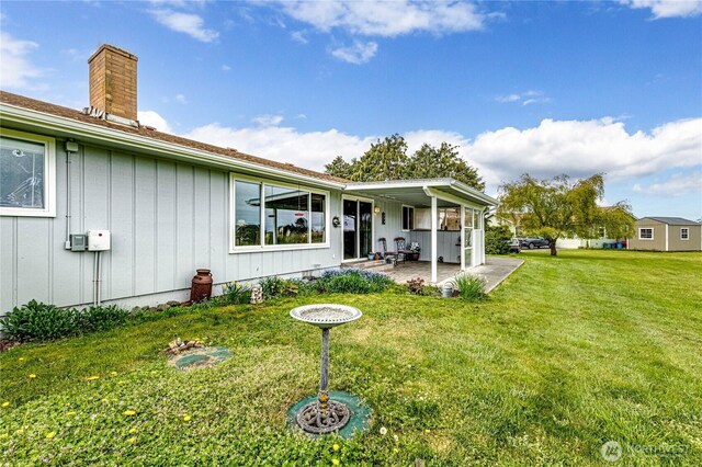 back of house with a lawn, board and batten siding, a chimney, and a patio area