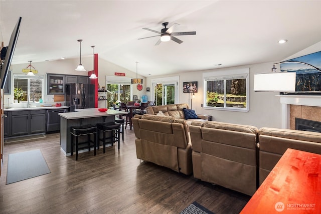 living area featuring a ceiling fan, dark wood-style flooring, a tiled fireplace, lofted ceiling, and recessed lighting