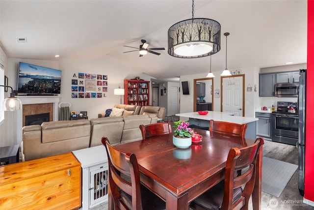 dining area with ceiling fan, visible vents, a fireplace, wood finished floors, and vaulted ceiling
