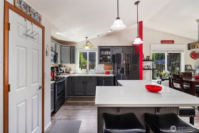 kitchen with a sink, a breakfast bar area, dark wood finished floors, vaulted ceiling, and black appliances