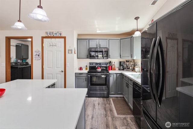 kitchen featuring gray cabinets, visible vents, washing machine and clothes dryer, wood finished floors, and black appliances