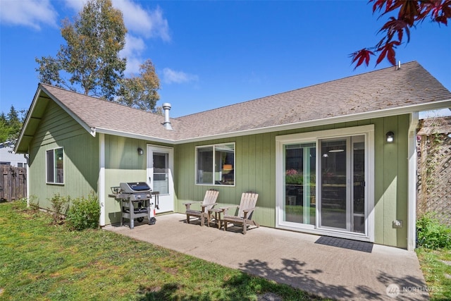back of property with a lawn, a shingled roof, and a patio area