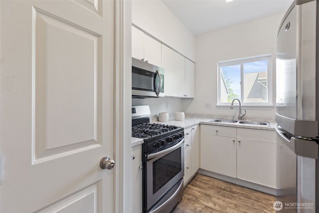 kitchen with stainless steel appliances, a sink, light wood finished floors, light countertops, and white cabinets
