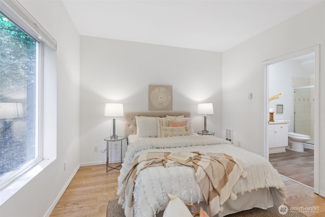 bedroom featuring multiple windows, light wood-type flooring, ensuite bath, and baseboards