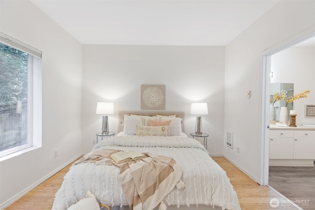 bedroom with baseboards, light wood finished floors, and ensuite bath