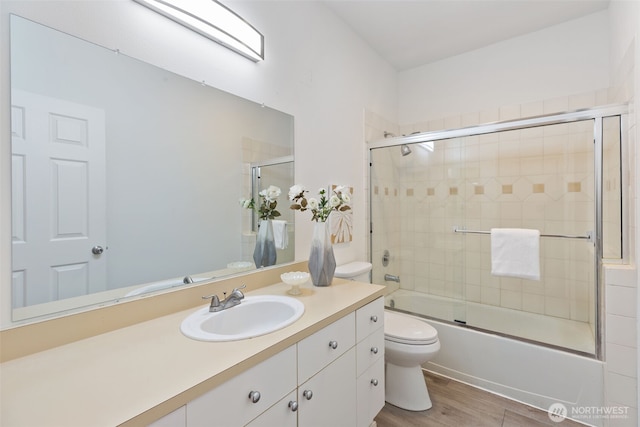 bathroom featuring toilet, wood finished floors, vanity, and bath / shower combo with glass door