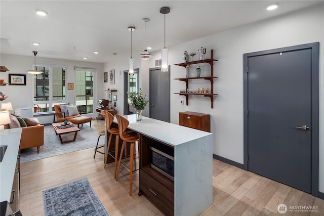kitchen featuring light wood-type flooring, pendant lighting, and stainless steel microwave