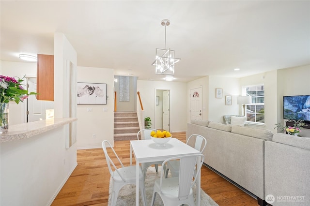 dining space featuring baseboards, light wood finished floors, stairs, and a notable chandelier