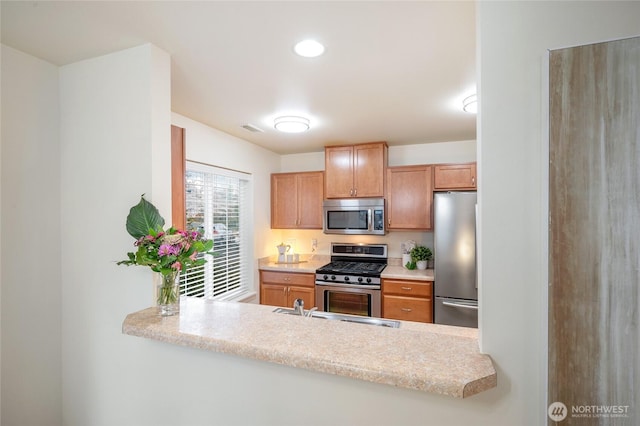 kitchen featuring appliances with stainless steel finishes, a sink, light countertops, a peninsula, and visible vents