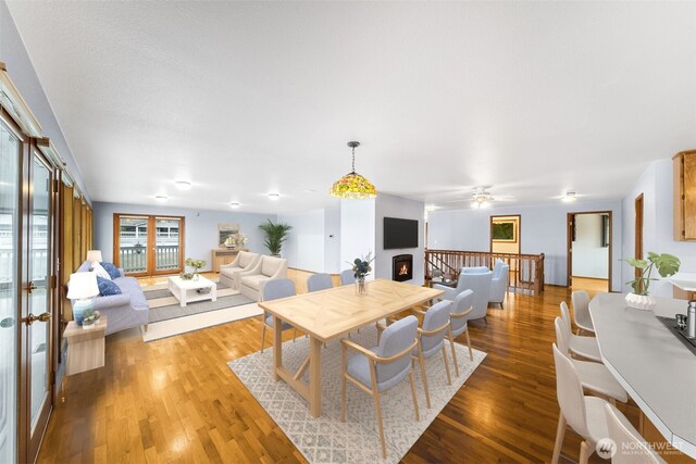 dining room featuring french doors, a ceiling fan, wood finished floors, and a warm lit fireplace