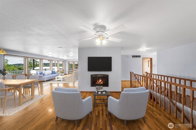 living room with visible vents, wood finished floors, ceiling fan, a lit fireplace, and a textured ceiling