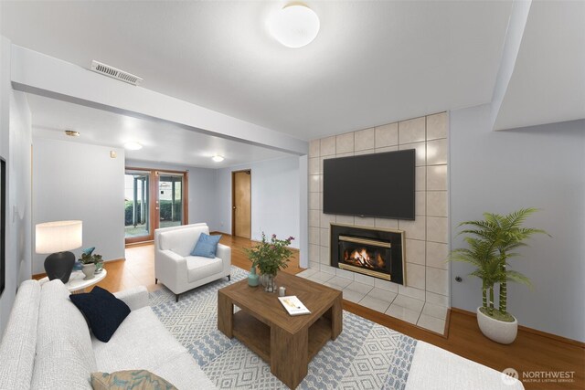 living area with visible vents, baseboards, wood finished floors, and a tile fireplace