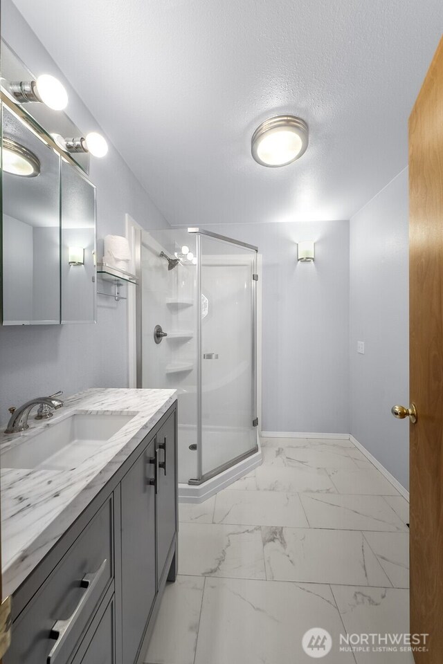 full bath featuring vanity, a textured ceiling, marble finish floor, baseboards, and a shower stall