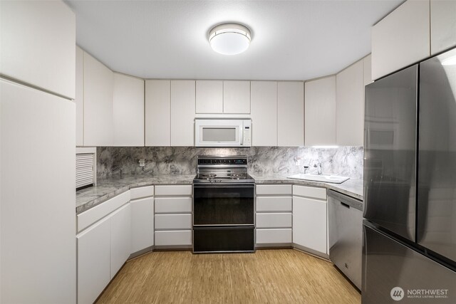kitchen with light wood-style floors, light countertops, white cabinets, a sink, and appliances with stainless steel finishes