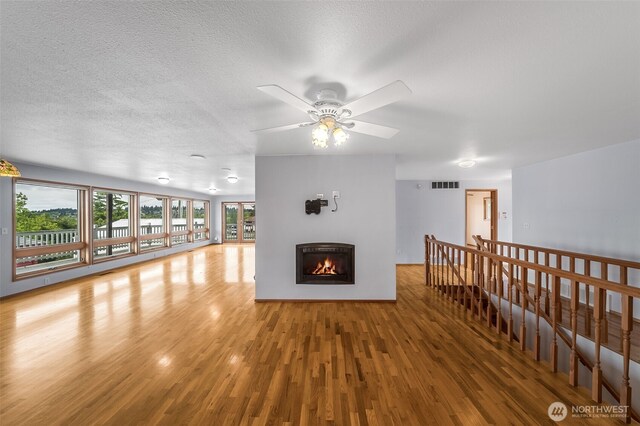 unfurnished living room featuring a textured ceiling, a glass covered fireplace, a ceiling fan, wood finished floors, and visible vents