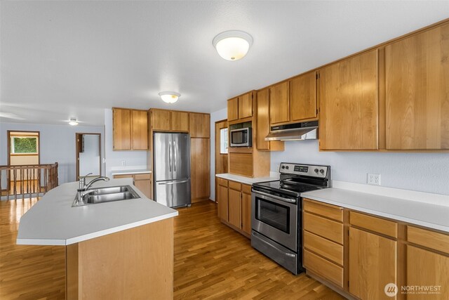 kitchen featuring appliances with stainless steel finishes, light wood-type flooring, a sink, light countertops, and under cabinet range hood
