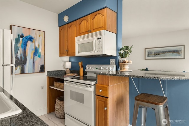 1156 Alki Ave SW Unit 401, Seattle, WA 98116 - kitchen with white appliances, brown cabinets, light tile patterned flooring, a kitchen breakfast bar, and dark stone counters