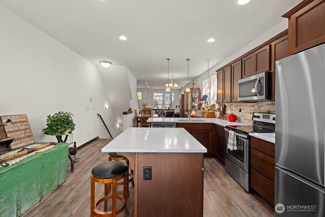 kitchen featuring a kitchen island, appliances with stainless steel finishes, a sink, a peninsula, and light wood-style flooring