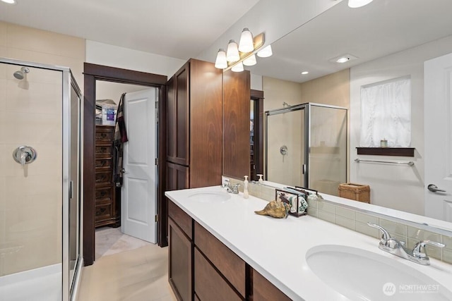 bathroom with double vanity, a spacious closet, a shower stall, and a sink