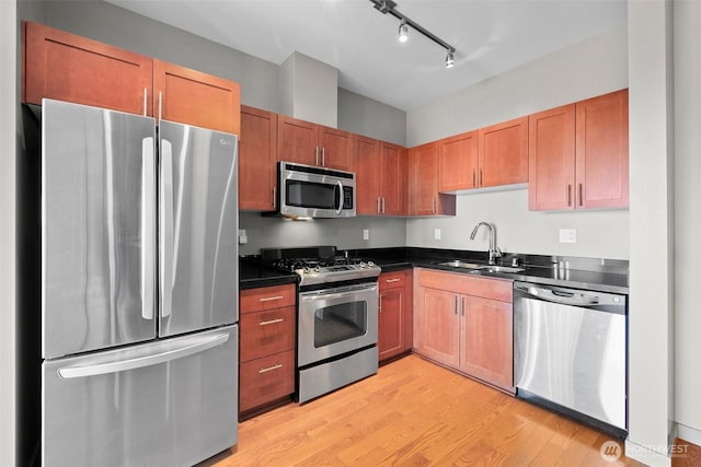 kitchen featuring appliances with stainless steel finishes, dark countertops, a sink, light wood-style floors, and track lighting