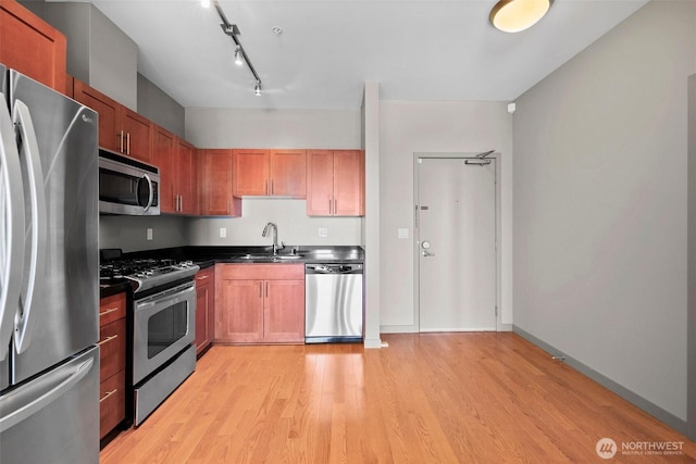 kitchen featuring appliances with stainless steel finishes, a sink, light wood-style flooring, dark countertops, and brown cabinets