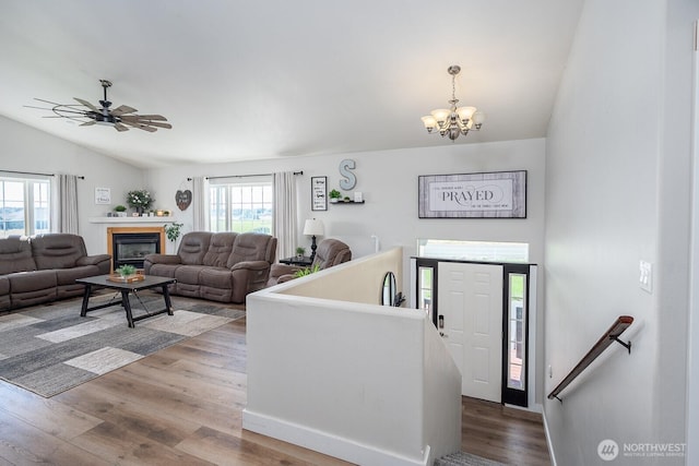 interior space featuring ceiling fan with notable chandelier, a glass covered fireplace, wood finished floors, and vaulted ceiling
