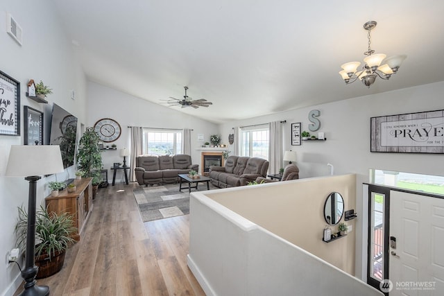 foyer featuring visible vents, a glass covered fireplace, wood finished floors, ceiling fan with notable chandelier, and vaulted ceiling