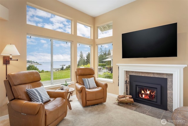 living room featuring a tiled fireplace, carpet, a towering ceiling, and baseboards