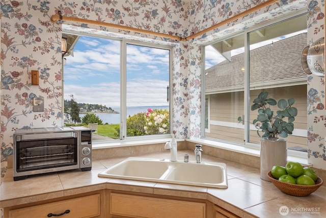 kitchen with wallpapered walls, a water view, and a sink