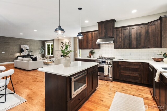 kitchen featuring light countertops, under cabinet range hood, dark brown cabinets, and stainless steel appliances