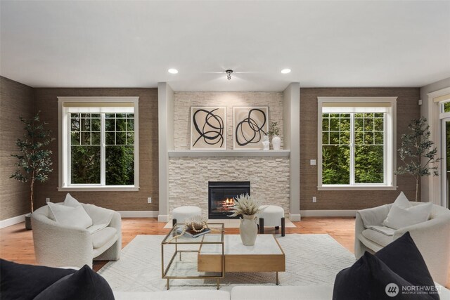 living area with recessed lighting, baseboards, light wood-type flooring, and a stone fireplace