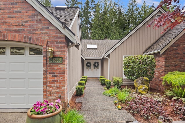 view of exterior entry with brick siding, an attached garage, and a shingled roof