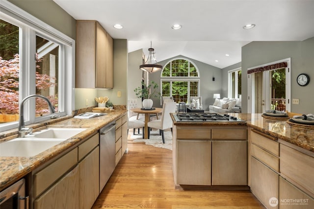 kitchen featuring appliances with stainless steel finishes, vaulted ceiling, a sink, light stone counters, and light wood-style floors