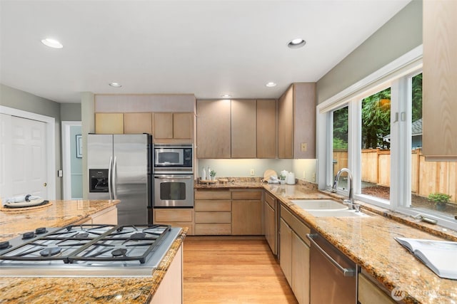 kitchen featuring light stone countertops, appliances with stainless steel finishes, a sink, light wood-style flooring, and recessed lighting