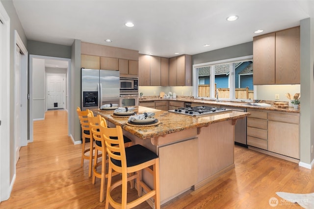 kitchen featuring light stone counters, light wood-style floors, stainless steel appliances, recessed lighting, and a kitchen bar