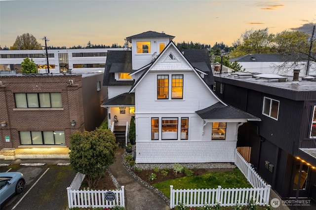 view of front facade featuring a fenced front yard, a shingled roof, and uncovered parking