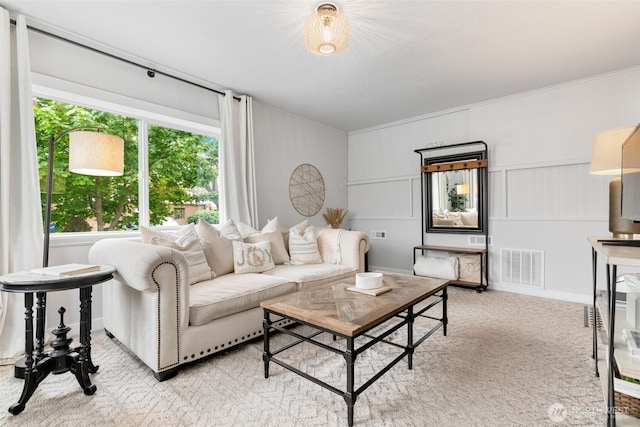 living area featuring visible vents, ornamental molding, a decorative wall, and light carpet