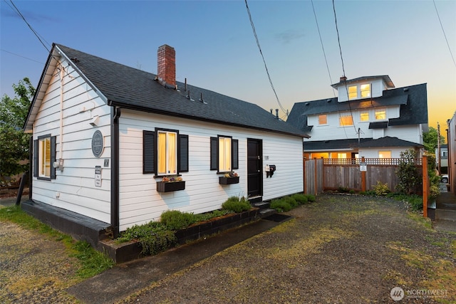 back of house at dusk featuring fence and a chimney