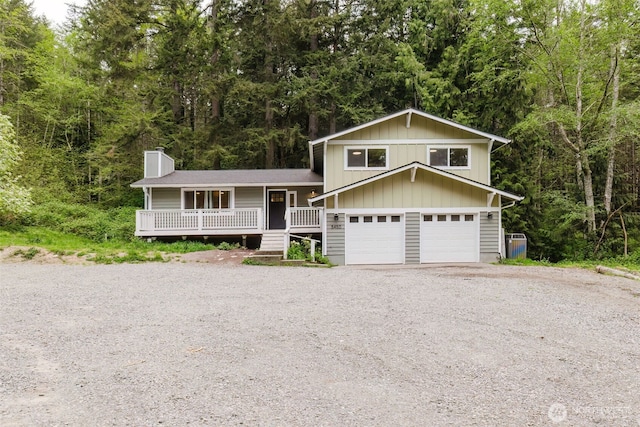 tri-level home with board and batten siding, a view of trees, a chimney, covered porch, and driveway