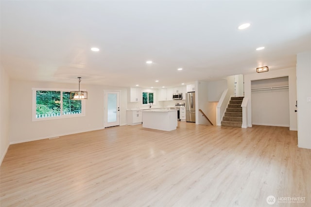 unfurnished living room with stairway, baseboards, recessed lighting, and light wood-style flooring