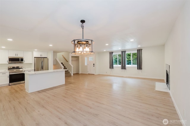 unfurnished living room with light wood-type flooring, stairs, baseboards, a notable chandelier, and recessed lighting
