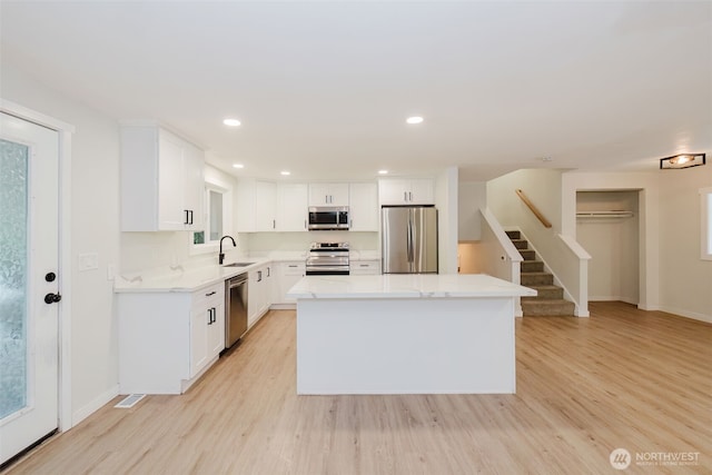kitchen with light wood-type flooring, a sink, appliances with stainless steel finishes, and a center island