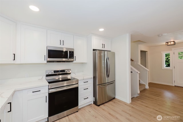 kitchen featuring appliances with stainless steel finishes, baseboards, white cabinets, light stone counters, and light wood finished floors