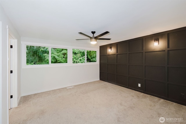 carpeted spare room featuring ceiling fan, baseboards, and a decorative wall