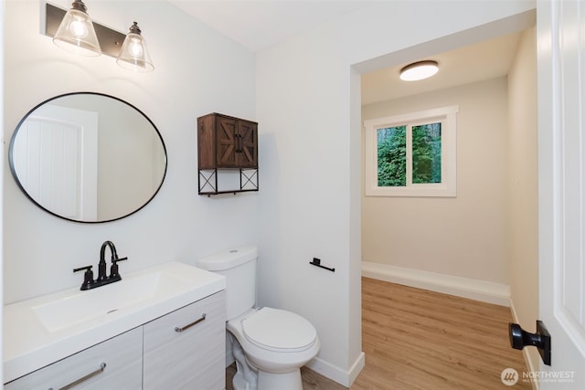 half bath featuring vanity, baseboards, toilet, and wood finished floors